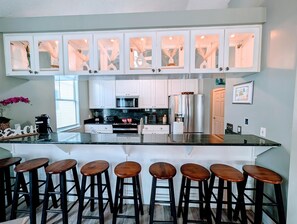 A kitchen with white cabinets, a black countertop, and a stainless steel refrigerator. There are six wooden stools around the island. - 60 Steps to Beach, Home with Private Pool and Separate Bungalow (Panama City)