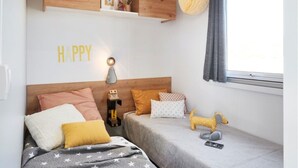 A cozy bedroom with a bed, a nightstand, a shelf with decorative items, a wall clock, and a window with curtains. - Carva - Confort 2 TV - 5p (57) (La Guérinière)