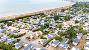 A large caravan park with numerous mobile homes, a beach in the background, and a clear sky. - Carva - Confort 2 TV - 5p (57) (La Guérinière)
