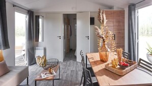 A modern living room with a sofa, a dining table with a vase and snacks, and a view of the outdoors through large windows. - Carva - Confort 2 TV - 5p (57) (La Guérinière)
