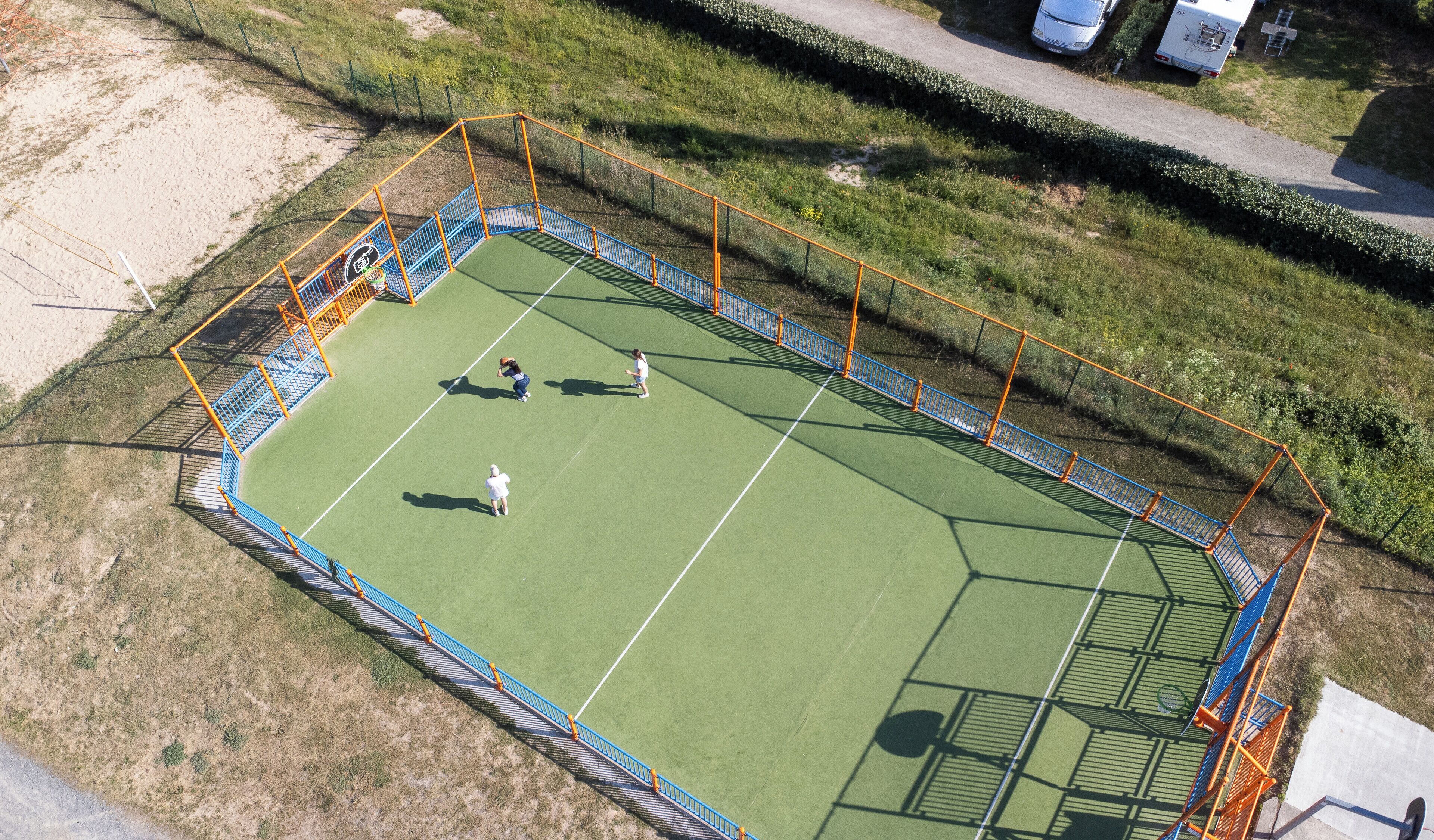 Una vista aerea di un campo da tennis con recinzione e aree verdi circostanti.