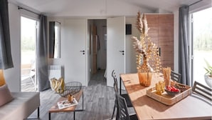 Ein modernes Wohnzimmer mit einer Couch, einem Esstisch mit einer Vase und Snacks sowie einem Blick ins Freie durch große Fenster.