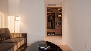 A modern living room with a sofa, a coffee table with books, and a walk-in closet with a robe and shoes. - Arden Hotel (Vancouver)