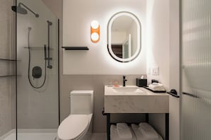 Un baño moderno con ducha de vidrio, inodoro, lavamanos y espejo con iluminación integrada.