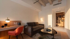 A modern living room with a sofa, a coffee table, a desk with a lamp, and a wardrobe. - Arden Hotel (Vancouver)