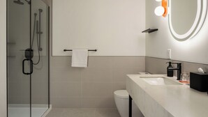 A modern bathroom with a glass shower enclosure, a white sink, and a mirror with lights. - Arden Hotel (Vancouver)