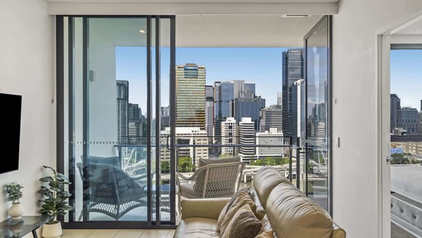 A modern living room with a large glass door leading to a balcony, offering a city view. - Central South Brisbane 2-Bed with Stunning Views (South Brisbane)