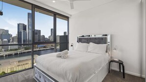 A modern bedroom with a large bed, a city view, and a ceiling fan. - Central South Brisbane 2-Bed with Stunning Views (South Brisbane)