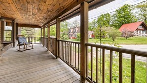 A wooden porch with a view of a red-roofed house and a blooming tree. - NEW! NH Getaway l HOT TUB l NearWhiteMountain (Campton)