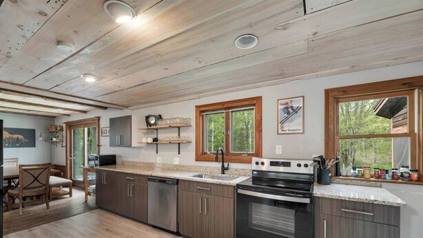 A modern kitchen with wooden cabinets, a stainless steel dishwasher, an oven, and a granite countertop. - NEW! NH Getaway l HOT TUB l NearWhiteMountain (Campton)
