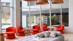 Un interior moderno con ventanas amplias, una zona de estar con mobiliario naranja y gris, y lámparas colgantes tejidas.