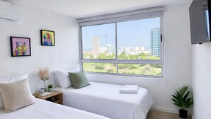 Una habitación de hotel moderna con dos camas, un ventanal con vistas a la ciudad y un televisor de pantalla plana montado en la pared.