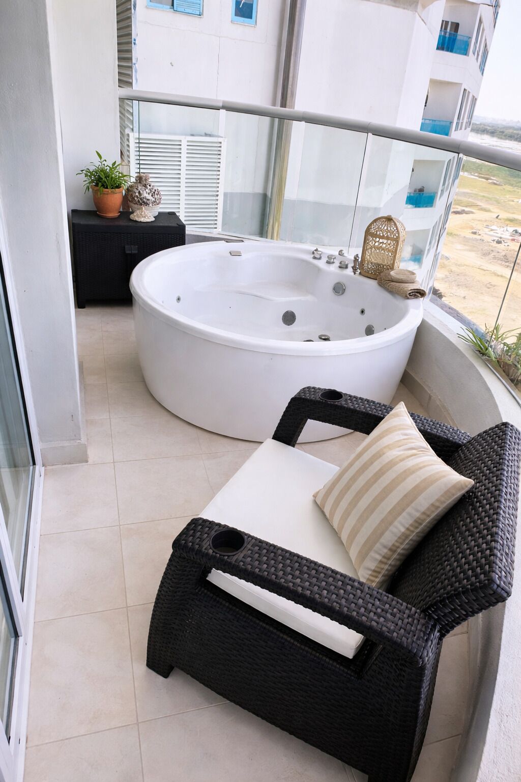 A balcony with a hot tub, wicker furniture, and a view of a building.