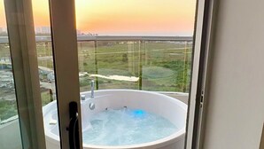 Een bubbelbad op een balkon met uitzicht op een zonsondergang en verre gebouwen.