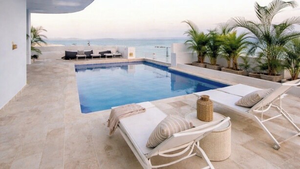 Un área de piscina moderna al aire libre con sillones de descanso y vistas al mar.