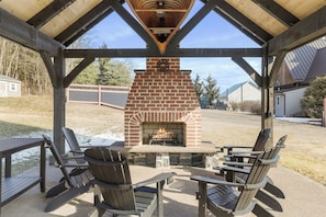 Un patio al aire libre con chimenea de ladrillo, sillas de madera y una mesa.
