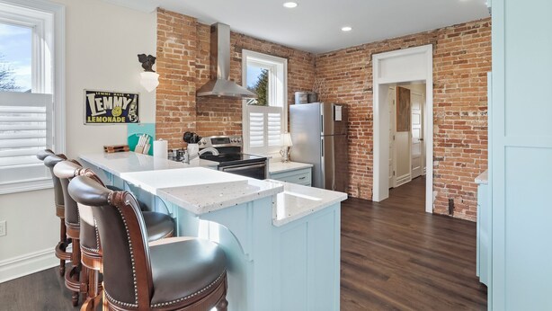 A kitchen with a brick wall, a large island with bar stools, a refrigerator, and a stove. - Clever Rabbit- Raystown Lake-Seven Points- Aunt Susies (Hesston)