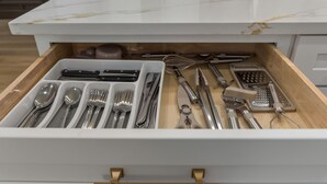 Uma gaveta com utensílios de cozinha bem organizados, incluindo colheres, garfos, facas e um ralador.