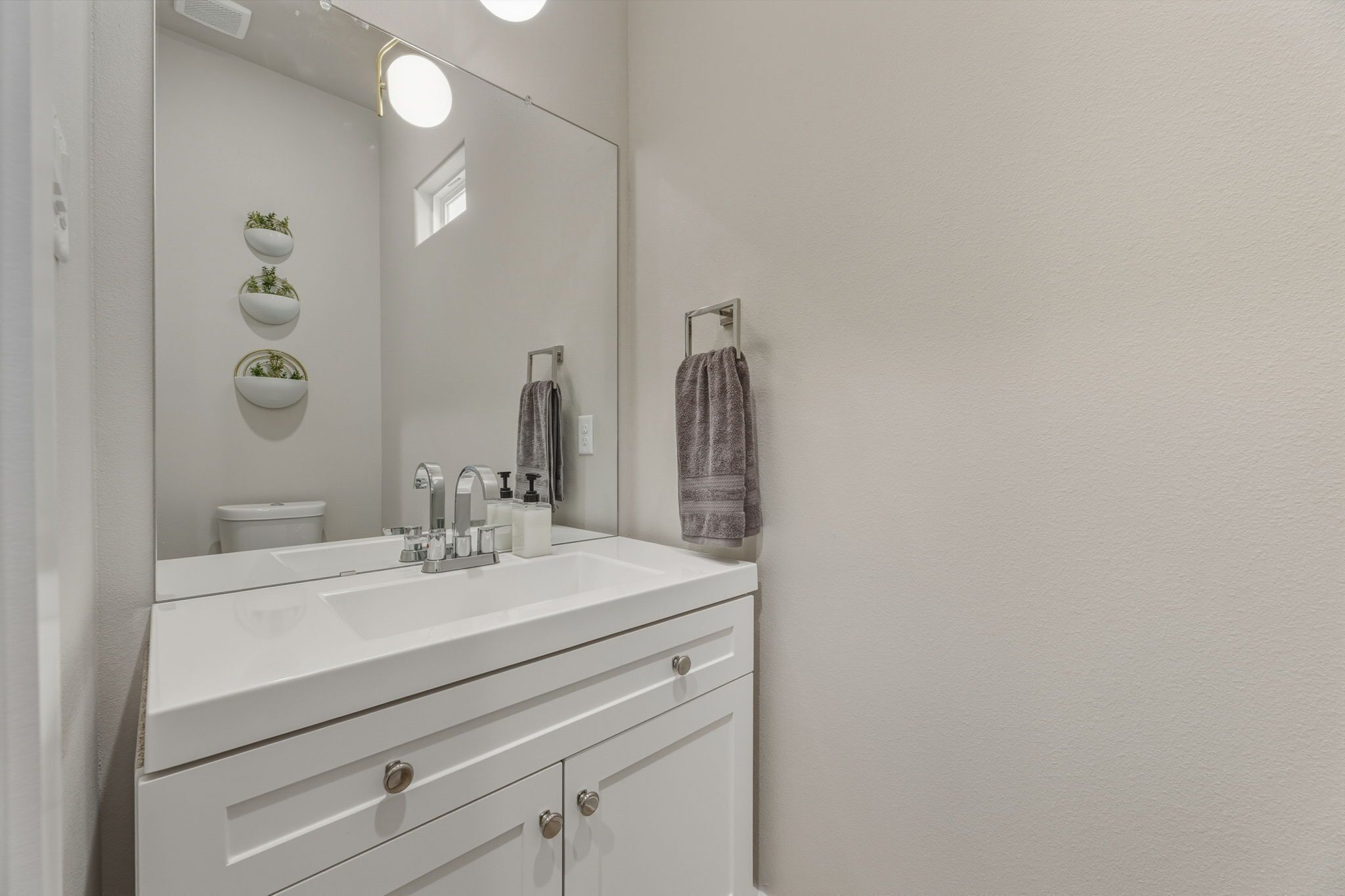 Une salle de bain avec un meuble-lavabo blanc, un grand miroir et trois jardinières fixées au mur.