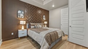 Quarto com cama, mesas de cabeceira, arte na parede e uma porta.