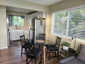 A compact kitchen with modern appliances, a dining area with a round table and chairs, and a window with blinds.