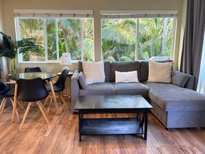 A living room with a sectional sofa, a coffee table, and a dining area with chairs and a table. - Oceanfront Hauula Home - North Unit B - 30+ Days (Hauula)