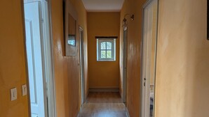 Een gang met houten vloeren en gele wanden, die uitkomt in een kamer met een raam.