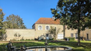 Een huis met een bakstenen gevel, een pannendak en een ronde fontein in de voortuin.