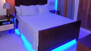 Ein Schlafzimmer mit einem Bett, Nachttischen, einem Deckenventilator und LED-Beleuchtung.