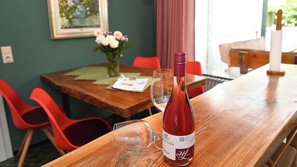 Una mesa de comedor con una botella de vino y una copa, sillas rojas, un florero con flores y un cuadro en la pared.