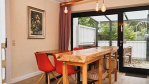 Un comedor con mesa de madera y sillas rojas, un cuadro en la pared y vistas al exterior por una puerta de vidrio.