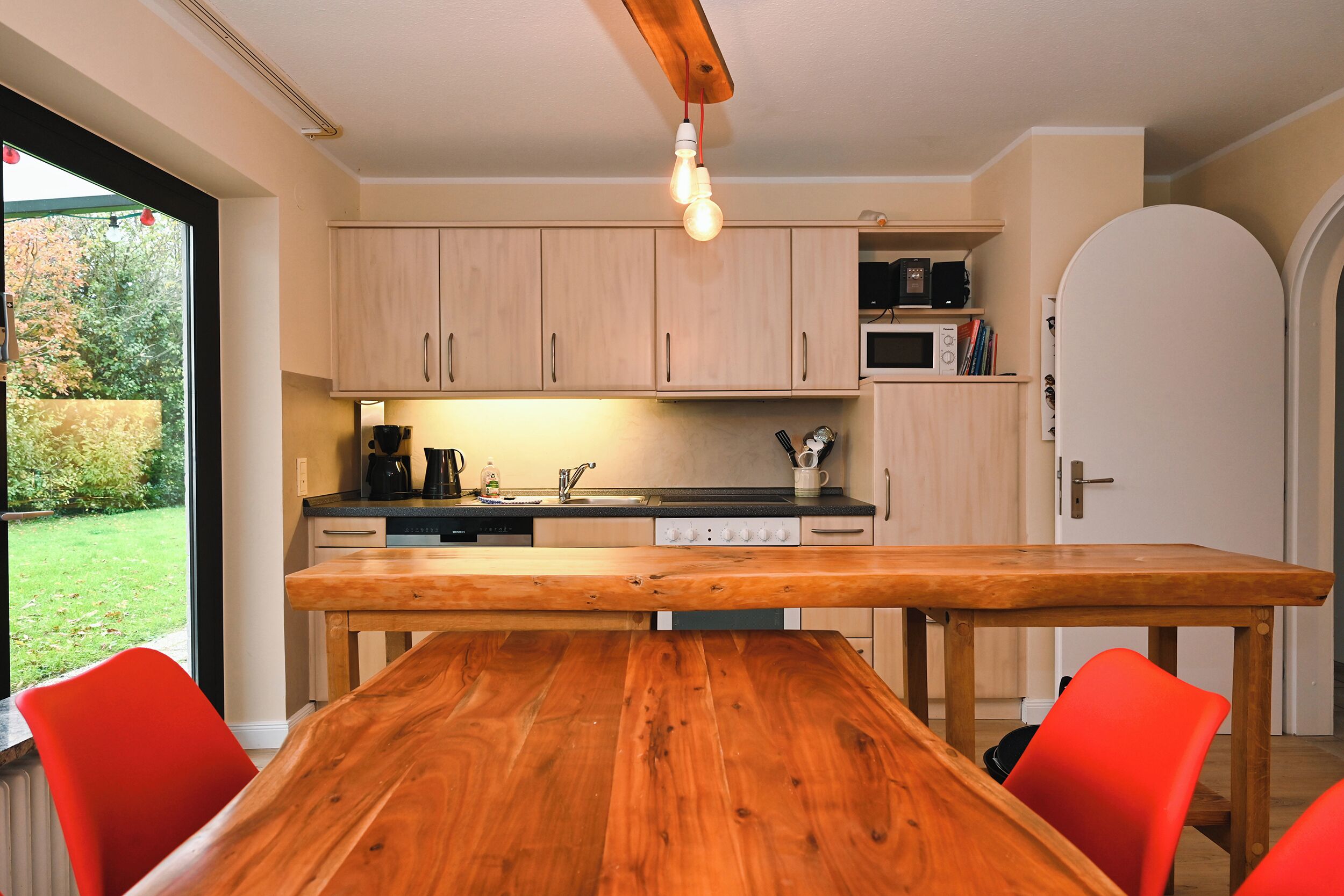 A modern kitchen with wooden cabinets, a built-in microwave, and a wooden dining table with red chairs.