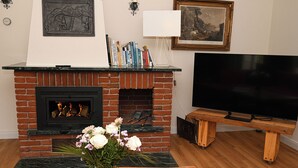 Una sala de estar con chimenea de ladrillo, un televisor de pantalla plana, una estantería y un jarrón con flores.