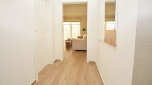 A narrow hallway with wooden flooring leading to a room with a bed and a window with curtains. - Watthof apartment 11<br>Modern apartment in a quiet location with access to the sea (Stinteck)