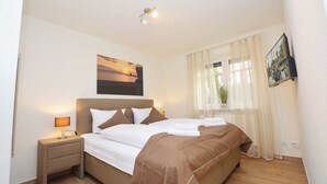 A neatly made bed with white and brown linens, a bedside lamp, and a framed picture above it. - Watthof apartment 11<br>Modern apartment in a quiet location with access to the sea (Stinteck)