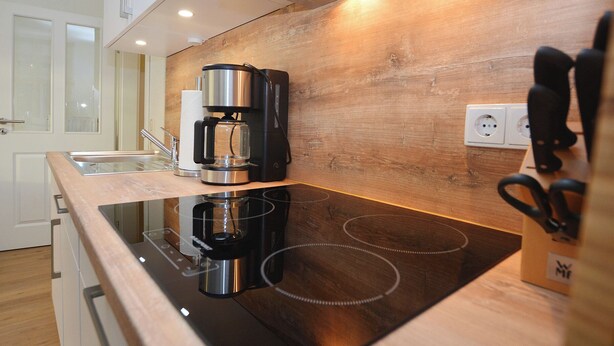 A modern kitchen with a wooden backsplash, a built-in stove, and a coffee maker. - Watthof apartment 11<br>Modern apartment in a quiet location with access to the sea (Stinteck)