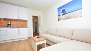 A compact living space with a kitchenette, a sofa, and a beach-themed wall art. - Watthof apartment 13<br>Cozy apartment with terrace and access to the sea time (Stinteck)