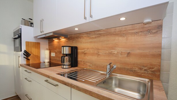 A modern kitchen with white cabinets, a wooden backsplash, a stainless steel sink, and a coffee maker. - Watthof apartment 13<br>Cozy apartment with terrace and access to the sea time (Stinteck)