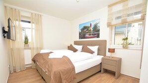 A bedroom with a bed, bedside table, lamp, and a window with a view of a harbor. - Watthof apartment 13<br>Cozy apartment with terrace and access to the sea time (Stinteck)