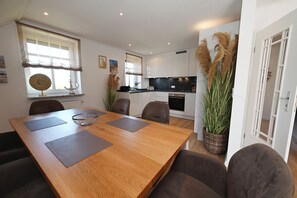 A modern kitchen with white cabinets, a black countertop, and a dining area with a wooden table and brown chairs. - Watthof 15 Apartment<br>: Modern duplex apartment with access to the ocean (Stinteck)