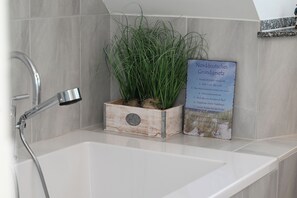 A bathroom with a white sink, a shower with a handheld showerhead, and a potted plant. - Watthof 15 Apartment<br>: Modern duplex apartment with access to the ocean (Stinteck)