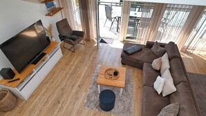 Un salon moderne doté d’un téléviseur à écran plat, d’un canapé marron, d’une table basse en bois et d’une grande fenêtre donnant sur l’extérieur.