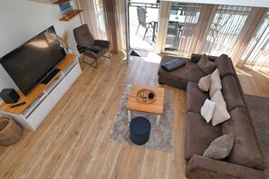 Un salon moderne doté d’un téléviseur à écran plat, d’un canapé marron, d’une table basse en bois et d’une grande fenêtre donnant sur l’extérieur.
