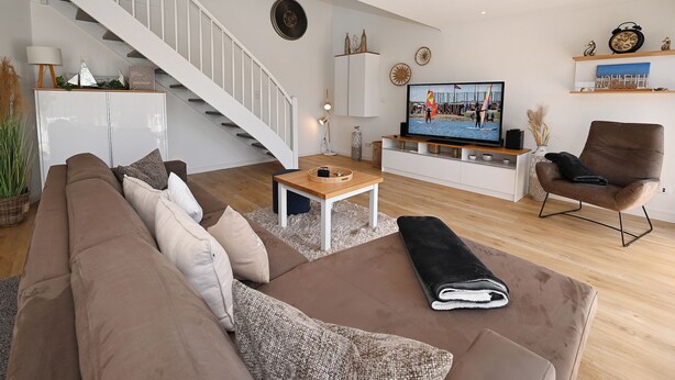 Un salon moderne avec un escalier, un téléviseur et un canapé marron.