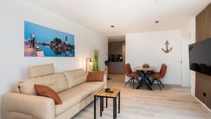 A modern living room with a sofa, a coffee table, and a dining area with chairs and a table. - Inseltörn apartment 10 (Büsum)