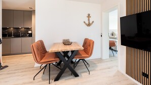 A modern dining area with a wooden table and two leather chairs, a kitchen in the background, and a TV mounted on the wall. - Inseltörn apartment 10 (Büsum)