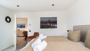 A spacious bedroom with a large bed, a brown chair, and a painting of a lighthouse at night. - Inseltörn apartment 10 (Büsum)