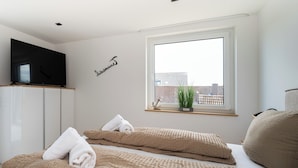 Ein modernes Hotelzimmer mit zwei Betten, einem Fernseher, einem Fenster mit Pflanze und einer Wand mit Namensschild.