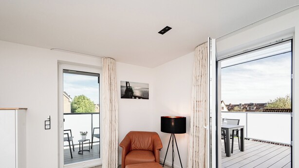 Ein modernes Wohnzimmer mit einer braunen Ledersofa, einer Stehlampe und einer Glastür, die auf eine Terrasse im Freien führt.