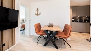 Ein moderner Essbereich mit einem Holztisch, zwei orangefarbenen Stühlen und einem an einer Holzvertäfelung befestigten Fernseher.